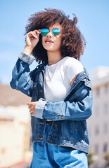 Poster - Woman, fashion and sunglasses outdoor in city for streetwear, summer and travel on a street. African person with natural hair or afro and urban background, glasses and jeans or clothes for freedom