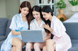 © Bangkok Click Studio - Three Asian cheerful happy female girlfriends in casual pajamas outfit sitting smiling watching surfing browsing internet online via laptop computer party together while drinking sparkling champagne
