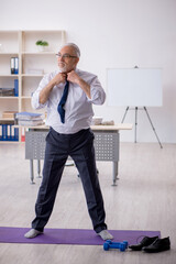 Wall Mural - Old male employee doing sport exercises at workplace