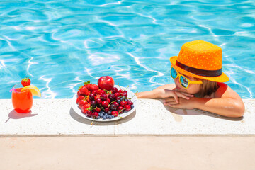 Wall Mural - Child eating fruits near swimming pool during summer holidays. Kids eat fruit outdoors. Healthy fruits for children.