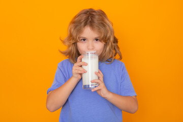 Wall Mural - Healthy food for kids. Child with a glass of milk. Cute boy in blue shirt holding glass of milk on yellow isolated studio background. Portrait of funny kid with milk mustache.