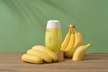 Wall Mural - A glass of banana juice placed on a wooden podium, decorated with bunches of banana. Bananas contains an abundance of vitamin A, which restores dull skin and helps brighten skin.