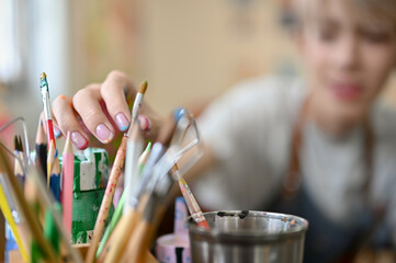 close-up image of a happy young asian gay man choosing paintbrush in a pencil stand