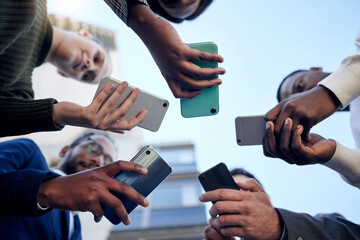 Wall Mural - Phone, low angle and group of business people networking in city outdoor. Smartphone, circle and team network together on social media, web email or online scroll on mobile app, tech or communication