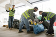 © LIGHTFIELD STUDIOS - Smiling female worker in high visibility vest and gloves putting plastic bag with trash near multiethnic colleagues in waste disposal station, garbage sorting and recycling concept