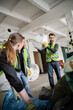 © LIGHTFIELD STUDIOS - Worker in protective vest and glove holding plastic bag with trash near blurred interracial colleagues working in waste disposal station, garbage sorting and recycling concept