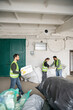 © LIGHTFIELD STUDIOS - Male worker in high visibility vest and gloves carrying foam plastic while interracial colleagues working with sacks in waste disposal station, garbage sorting and recycling concept