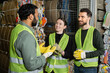 © LIGHTFIELD STUDIOS - Indian worker in high visibility vest and gloves talking to smiling colleagues while standing near waste paper in blurred garbage sorting center, waste sorting and recycling concept