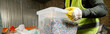 © LIGHTFIELD STUDIOS - Cropped view of sorter in protective vest and glove holding container with plastic for recycle while working in blurred garbage sorting center, garbage sorting and recycling concept, banner