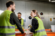 © LIGHTFIELD STUDIOS - Smiling woman in protective uniform and gloves holding garbage and talking to interracial colleagues while working together near conveyor in waste disposal station, garbage sorting concept