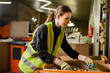 © LIGHTFIELD STUDIOS - Young female worker of garbage sorting center wearing protective clothing and gloves while working with plastic caps in carton boxes, garbage sorting and recycling concept