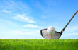 Golf ball on tee and driver golf club with blue sky background.