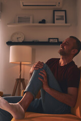 Man with knee pain sitting on a sofa at home.