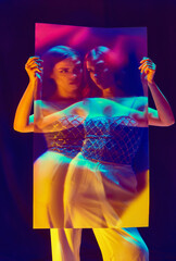 Charming fashion model, young girl wearing elegant clothes posing over violet background in neon light. Blurred effect. Mirror reflection