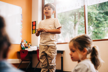 Wall Mural - Confident little boy stands in front of his class to give a speech