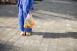 Woman in slippers carrying mesh bag full of fresh fruits and vegetables while walking home, close-up. Sustainable lifestyle and using reusable bag in shopping food concept