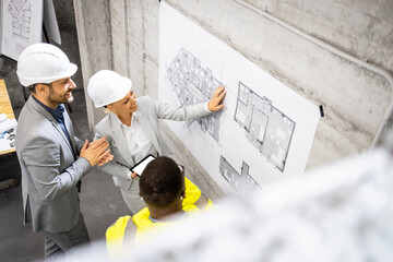 Group of architects and building workers having a meeting, discussing blueprint. Construction site interior.