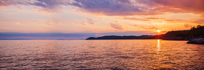 Wall Mural - Breathtaking panoramic view of the rocky beach at twilight, a dramatic sky and golden horizon reflected on tranquil sea waters, with colorful summer sunshine.