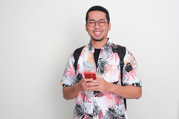 Wall Mural - Asian tourist smiling happy while holding mobile phone and wearing backpack