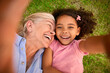 © Monkey Business - POV Overhead Shot Of Grandmother And Granddaughter Lying On Grass Taking Selfie On Mobile Phone