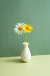 Vase of white and yellow flower on table. green wall background. minimal object