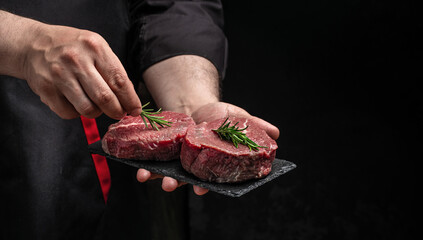 Poster - male hands holding beef meat on a dark background, Whole piece of tenderloin with steaks and spices ready to cook, Long banner format