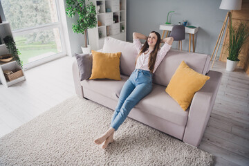 Wall Mural - Photo of charming dreamy young lady dressed striped shirt lying sofa arms behind head having rest indoors house room