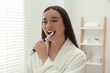 © New Africa - Young woman brushing her teeth with electric toothbrush in bathroom