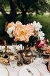 coral and white peonies in an iron vase on the table. holiday outdoors. details of a table decorated with a bouquet of peonies. table setting example.