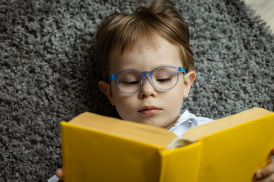 Wall Mural - child with glasses reading a book lying on the floor, vision correction, myopia concept