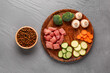 Bowl with dry pet food, raw meat and natural products on color wooden background
