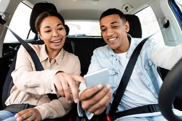 Happy black woman and man looking for way on map on cellphone while driving in car, using digital map application. Weekend trip and journey together