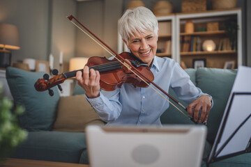 Mature senior caucasian woman learn to play violin practice at home