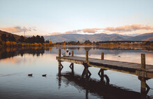 Wide Shot Of A Woman Sitting On A Pier Playing The Guitar In Cromwell, New Zealand