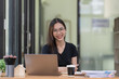 © Songsak C - Portrait of a young beautiful Asian woman smiling and looking at the camera while sitting at her office desk.