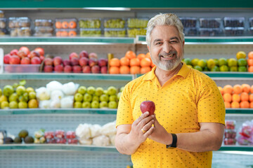 Senior indian man showing apple fruit at fruit shop. Healthy lifestyle concept.