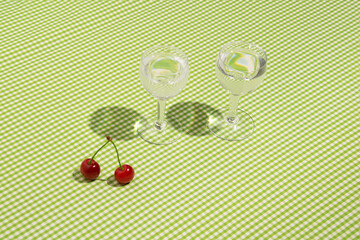 Two glasses of fruit liqueur, cherries, retro style checkered green pattern background. Nostalgia girls party idea. 