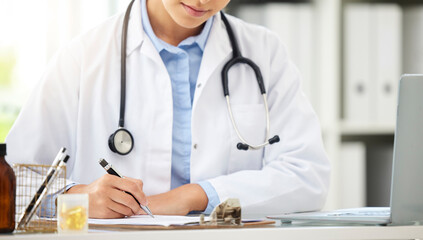 Wall Mural - Planning, doctor writing on a clipboard and with laptop at a desk in a modern office with lens flare. Healthcare, medical research and female nurse or surgeon with stethoscope write notes at work