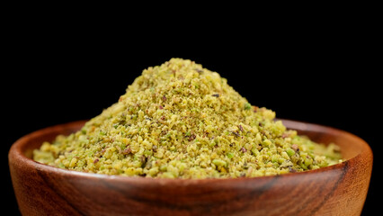 Wall Mural - Pistachio flour in wooden bowl, black background. Ground pistachio ingredient for dessert and bakery product