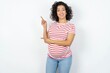 © Roquillo - Beautiful pregnant woman wearing striped T-shirt standing over white studio background indicating finger empty space showing best low prices, looking at the camera