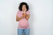 © Roquillo - Joyous Beautiful pregnant woman wearing striped T-shirt poses with mobile phone device, types text message on modern smartphone, watches funny video during free time, enjoys good internet connection,