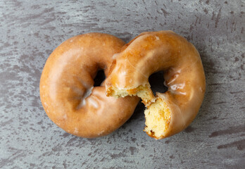 Wall Mural - Top view of a bitten and whole freshly baked cake donut on a gray mottled countertop.