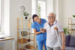 © Studio Romantic - Friendly female nurse helping a disabled retired senior man walk with a crutch, holding him by the elbow, supporting and reassuring him. Senior care, assisted living, disability, injury concept