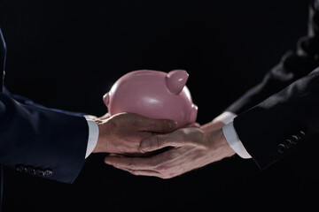 A businessman gives you a piggy bank isolated on a black background.