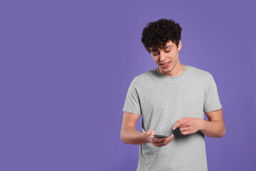 Wall Mural - Handsome young man using smartphone on violet background. Space for text