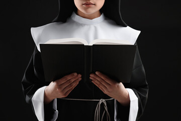 Nun reading Bible on black background, closeup