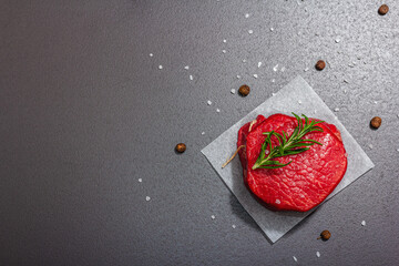 Wall Mural - Raw Ribeye steak with spices and herbs on black stone background. Trendy hard light, dark shadow