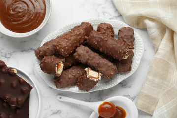 Tasty chocolate bars with caramel on white marble table, flat lay