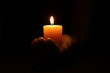 © New Africa - Woman holding burning candle in hand on black background, closeup