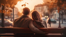 Young Couple In Love Sitting On A Bench Against Sunrise With A City View
